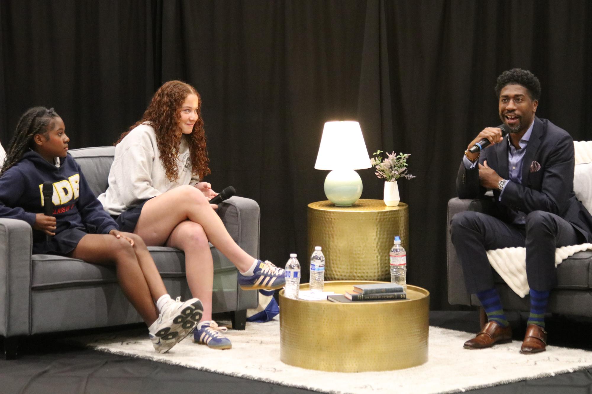  Dr. Lerone Martin sitting on stage with discussion leaders, sophomores Vivienne Butler and Aria Smith.
