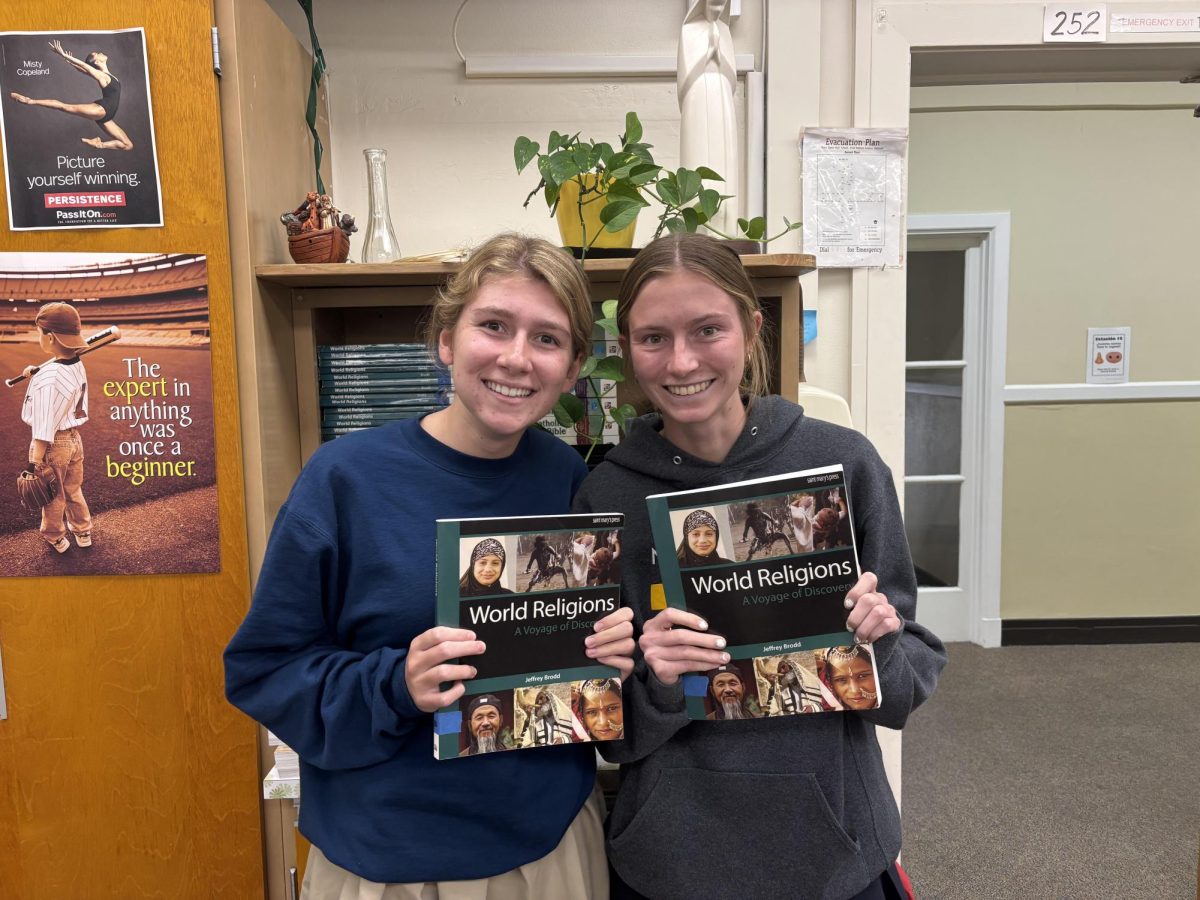 Seniors Maisie Street and Avery Jones holding up the World Religions textbook