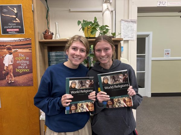 Seniors Maisie Street and Avery Jones holding up the World Religions textbook