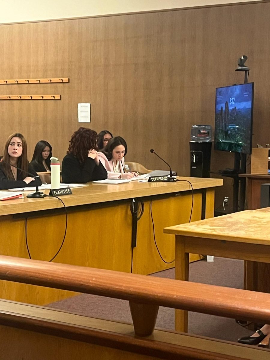 Varsity defense attorneys writing notes to each other during the prosecutions opening statements.