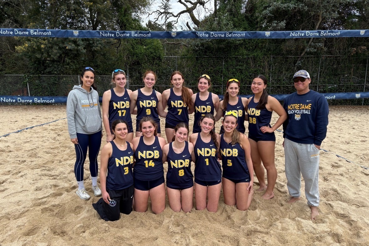 The beach volleyball team posing for a photo on the sand courts. 